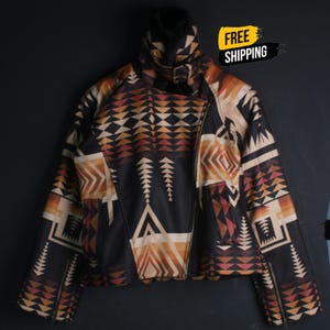 May include: A long-sleeve jacket featuring a black, tan, and rust-colored geometric pattern. The jacket has a high collar with a buckle strap, an asymmetrical front zipper closure, and zippered cuffs. The design includes repeating triangles.