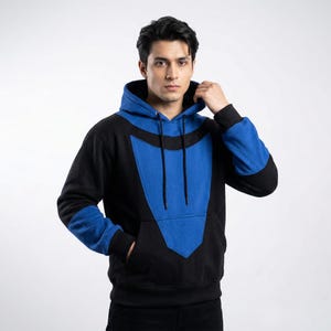 May include: Black and blue hooded sweatshirt with a front pocket. The sweatshirt has a striking blue design on the front and sleeves, with black detailing. The person is wearing the sweatshirt and has their hand in the pocket.