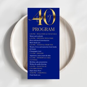 May include: A navy blue event program with gold lettering and a gold "40" graphic. The program includes a schedule of events, such as welcome cocktails, dinner, and dancing. The program is displayed on a white wooden plate.