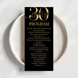 Op de afbeelding: Een zwart 30e verjaardagsprogramma-kaartje met gouden tekst. Het programma bevat het schema voor de avond, zoals welkom, diner, toosten en dansen. De kaart wordt weergegeven op een wit bord.