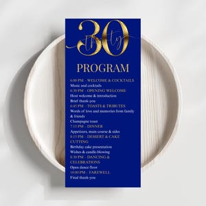 May include: A navy blue event program for a 30th birthday celebration. The program features gold script text and a detailed schedule of events, including dinner, toasts, and dancing. The program is displayed on a white plate.