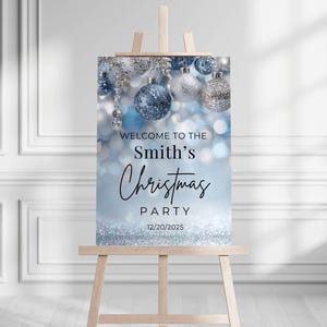 May include: A rectangular sign on a wooden easel featuring a blue and silver holiday theme with hanging ornaments. The text reads: WELCOME TO THE Smith's Christmas PARTY 12/20/2025. The background displays a soft-focus bokeh effect with glittery accents.