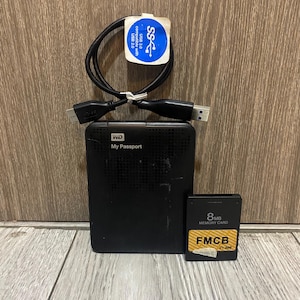 May include: A black WD My Passport external hard drive, a black 8MB memory card, and a black USB cable with a white label. The memory card has the text "8MB MEMORY CARD" and "FMCB V1.986". The USB cable has a white label with the text "USB 3.0 compatible with USB 2.0".
