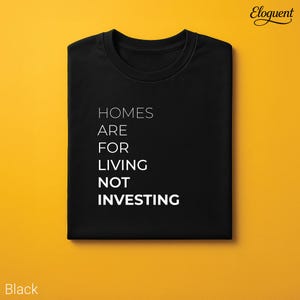 May include: A black crew neck t-shirt featuring the white text HOMES ARE FOR LIVING NOT INVESTING printed on the front. The shirt is folded neatly and displayed against a solid yellow background. The word Eloquent appears in the top right corner.
