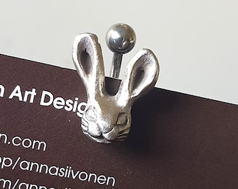 May include: A silver-colored belly button ring featuring a detailed rabbit head design. The rabbit's ears are upright, and the ring has a small ball on top. The ring is displayed on a brown card with text.
