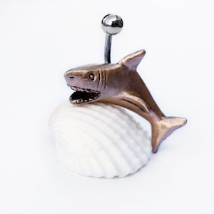 May include: A gold shark figurine on a white seashell with a silver top.