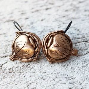 Pode incluir: Um par de brincos de bronze em forma de olho fechado com veias detalhadas e um gancho de arame preto.