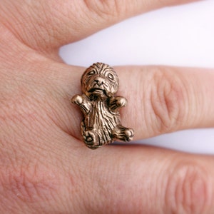 May include: A gold-toned ring featuring a detailed sculpture of a small dog sitting with its paws raised.