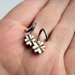 May include: A pair of silver earrings with a four-leaf clover design. The earrings are made of metal and have a black finish.