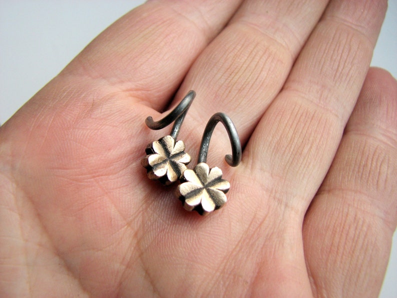 May include: A pair of silver earrings with a four-leaf clover design. The earrings are made of metal and have a black finish.