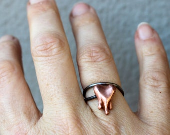 May include: A silver ring with a copper heart-shaped charm. The charm is dripping with copper, giving it a melted look.
