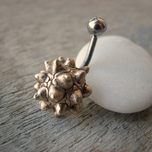 Op de afbeelding: Een zilveren navelpiercing met een gouden, stekelige, stervormige bedel.