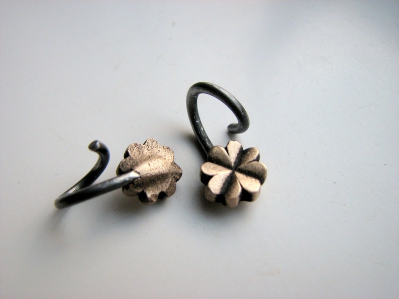 May include: Two silver earrings with a gold four-leaf clover charm.