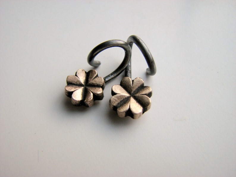 May include: A pair of silver earrings with a four-leaf clover design in gold.