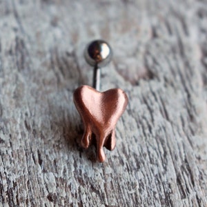 May include: A copper-colored heart-shaped body piercing with a silver ball on the top. The heart is dripping with a melted effect.