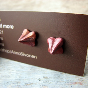 May include: A pair of small, pink heart-shaped earrings made of metal. The earrings are on a brown card with the text "Silvonen Jewellery and more" printed on it.
