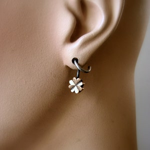 May include: A silver hoop earring with a small, gold-colored four-leaf clover charm hanging from it.