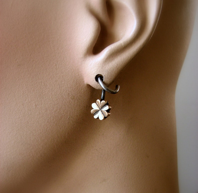 May include: A silver hoop earring with a small, gold-colored four-leaf clover charm hanging from it.