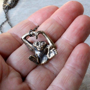 Puede incluir: Un collar de bronce con un dije de mono en forma de coraz&oacute;n. El mono est&aacute; sosteniendo sus manos juntas para formar un coraz&oacute;n.