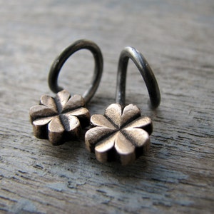 May include: A pair of silver earrings with a four-leaf clover design in gold. The earrings are made of a thin wire that is twisted into a loop.