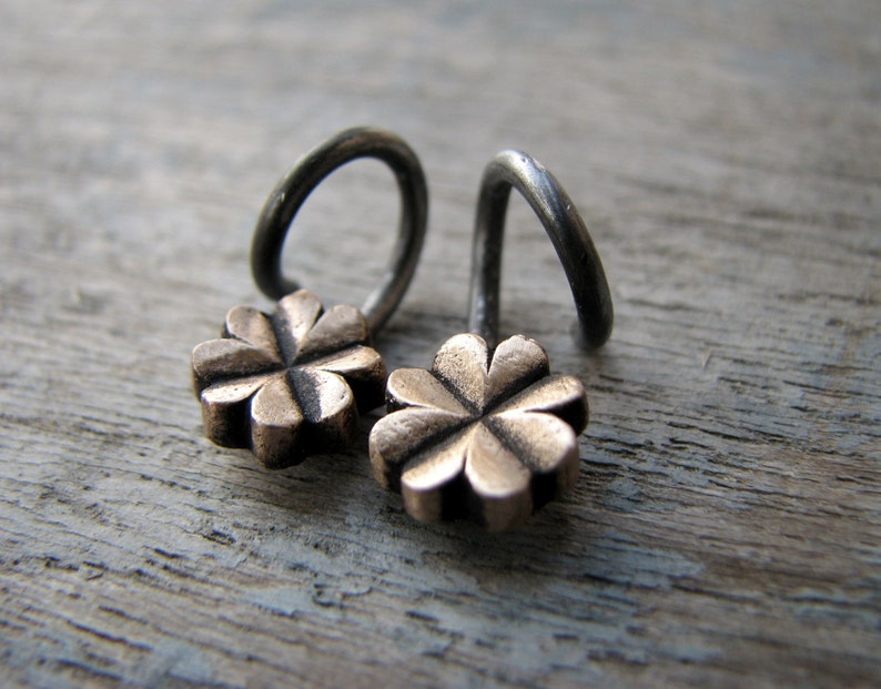 May include: A pair of silver earrings with a four-leaf clover design in gold. The earrings are made of a thin wire that is twisted into a loop.
