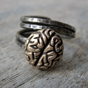 May include: A silver ring with a textured band and a gold brain-shaped design.