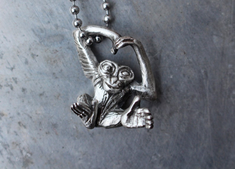 Puede incluir: Collar con colgante de mono de plata con un dise&ntilde;o detallado. El mono est&aacute; colgado de una cadena con los brazos levantados por encima de su cabeza.