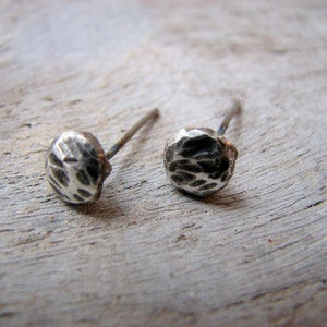 May include: A pair of silver stud earrings with a hammered texture. The earrings are small and round, and they have a simple, minimalist design.