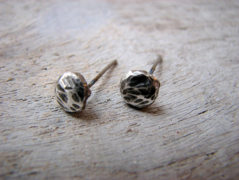 May include: A pair of silver stud earrings with a hammered texture. The earrings are small and round, and they have a simple, minimalist design.
