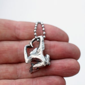 Puede incluir: P&eacute;ndulo de plata con forma de mono con un dise&ntilde;o detallado. El mono est&aacute; agarrado a una cadena con sus brazos y piernas. El colgante est&aacute; colgado de una cadena de plata.