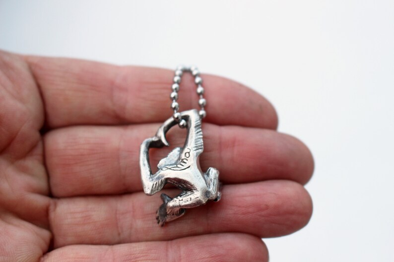 Puede incluir: P&eacute;ndulo de plata con forma de mono con un dise&ntilde;o detallado. El mono est&aacute; agarrado a una cadena con sus brazos y piernas. El colgante est&aacute; colgado de una cadena de plata.