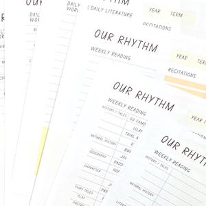 May include: A close-up of a white planner with the words "Our Rhythm" written in black. The planner is divided into sections for weekly reading, history, tales, natural history, geography, character, fairy tales, play, and poetry. The planner also includes sections for daily literature, daily work, year, and term.