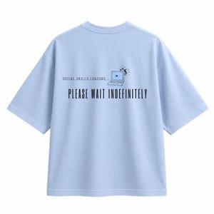 May include: A light blue short-sleeve t-shirt featuring a graphic of a laptop with a loading icon and the text "SOCIAL SKILLS LOADING..." above the larger black text "PLEASE WAIT INDEFINITELY" printed on the back of the garment.