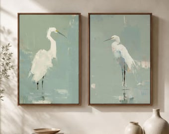 May include: A set of two framed wall art prints featuring white egrets against a muted sage green background. Each rectangular canvas displays a bird in a standing position with visible brushstroke textures, enclosed in a thin brown frame.
