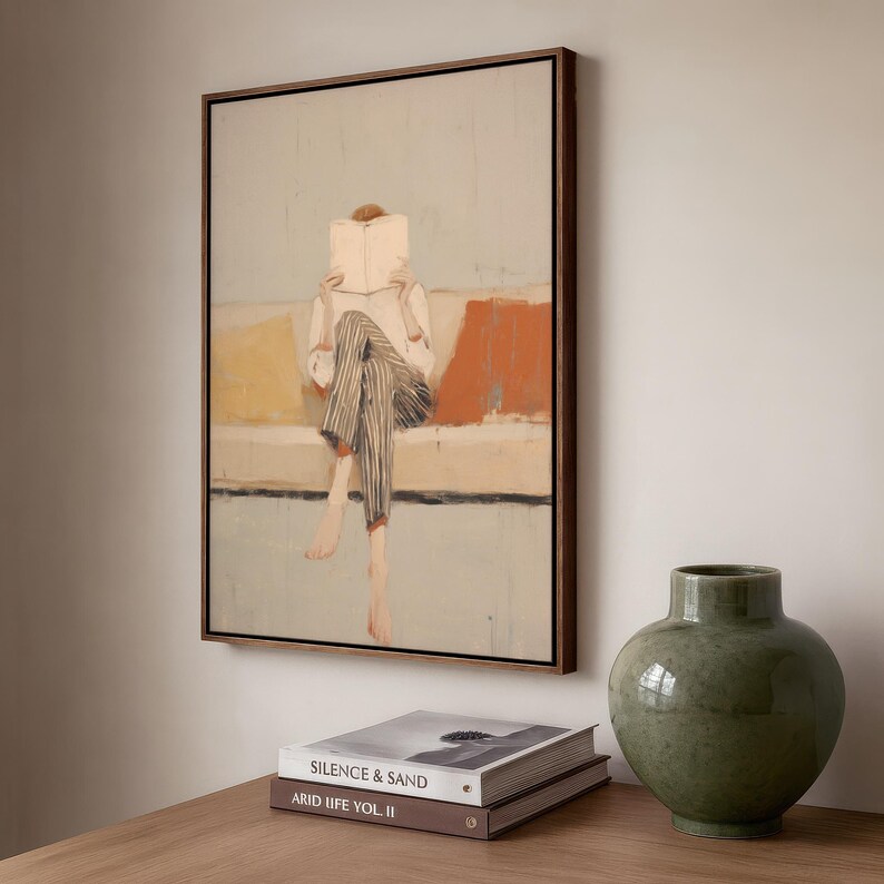May include: An abstract painting in a wooden frame shows a person reading a book. The artwork features a person in striped trousers and a white shirt, with a light blue, yellow, and orange background. A green vase and books are in the foreground.