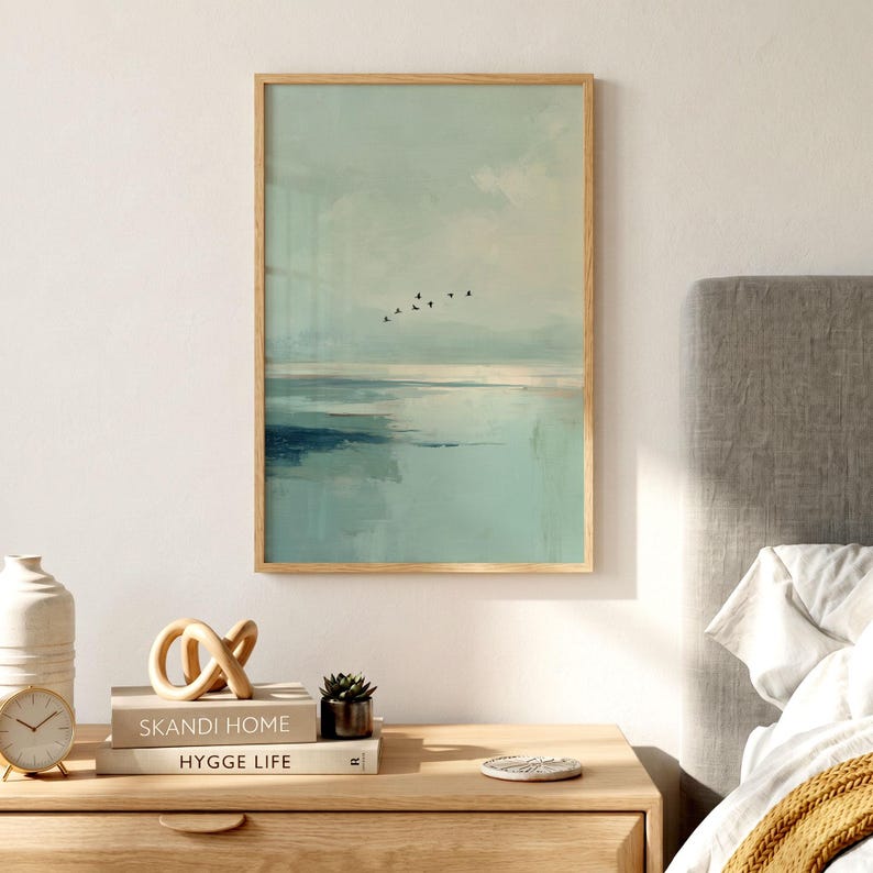 May include: A vertical rectangular wall art print in a light wood frame featuring an abstract landscape painting with soft sage green and blue tones, depicting a calm horizon line and a small flock of black birds flying across the sky.