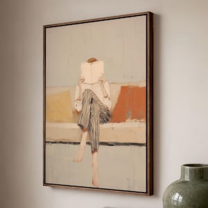 May include: An abstract painting in a dark wood frame shows a person reading on a sofa. The person is wearing striped trousers and a white shirt. The background features muted colours of orange, yellow, and blue.
