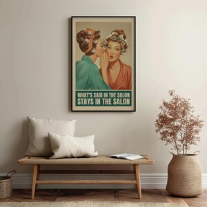 May include: A framed vintage-style poster featuring two women in curlers, one whispering to the other. The poster has the text "WHAT'S SAID IN THE SALON STAYS IN THE SALON" in a green box. The poster is displayed above a wooden bench with pillows.