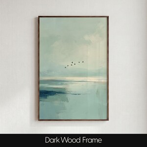 May include: A vertical wall art print in a dark wood frame featuring a soft, abstract landscape painting. The scene depicts a calm, light blue and teal water surface under a hazy sky with a small flock of black birds flying in the distance.