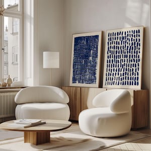 May include: Two framed rectangular wall art prints featuring dark blue abstract patterns on a light background. One print displays a dense grid of horizontal and vertical lines, while the other shows a series of vertical, dashed brushstrokes.