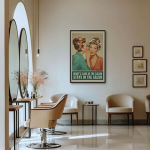 May include: A framed vintage-style poster with the text "WHAT'S SAID IN THE SALON STAYS IN THE SALON" hangs on a wall. The poster depicts two women in curlers, one whispering to the other. The salon interior features mirrors, chairs, and a table.