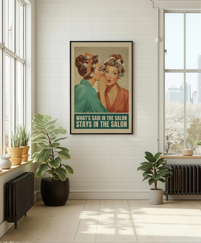 May include: A framed vintage-style poster featuring two women in curlers, one whispering to the other. The poster has the text "WHAT'S SAID IN THE SALON STAYS IN THE SALON" in a green box. The image is in a bright room with plants.