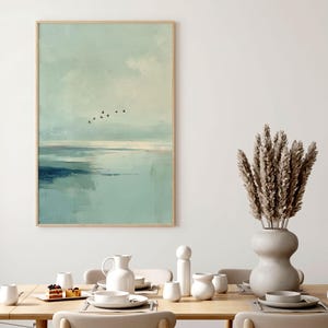 May include: A framed vertical wall art print depicting a serene landscape with a pale blue and teal sky, a calm body of water, and a small flock of black birds flying in the distance. The artwork features soft, blended brushstrokes and muted tones.
