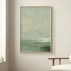 May include: A framed landscape painting in muted greens and off-white tones. The artwork shows a seascape with a flock of birds in flight. The wooden frame complements the artwork's natural aesthetic, suitable for home decor.