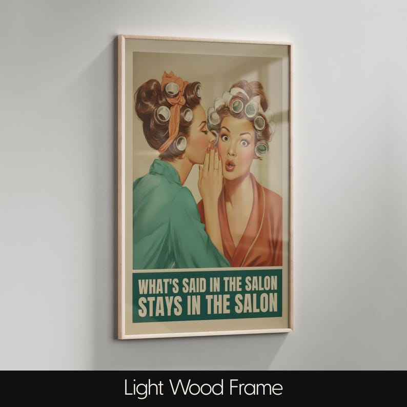 May include: Framed vintage-style print featuring two women in curlers. One whispers to the other, who looks shocked. The print has a green banner with the text "WHAT'S SAID IN THE SALON STAYS IN THE SALON". The frame is light wood.