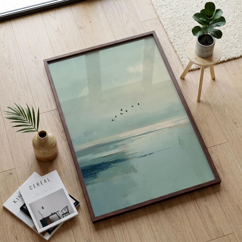 May include: A rectangular framed wall art print featuring an abstract landscape in shades of pale green, blue, and white, with a small flock of black birds flying across the center. The artwork is encased in a dark brown wooden frame.
