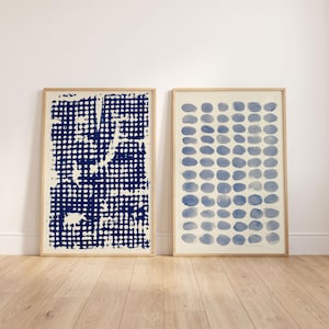 May include: Two framed rectangular wall art prints. The left print features a dark blue grid pattern with irregular white gaps. The right print displays a vertical arrangement of light blue circular shapes in a grid, both set in light wood frames.