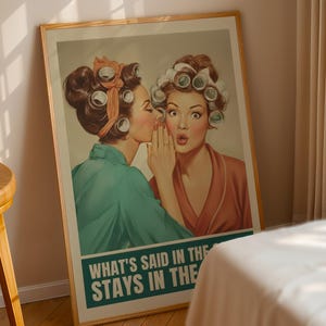 May include: A framed vintage-style poster featuring two women with curlers in their hair. One whispers to the other, who looks surprised. The poster has a teal and white banner at the bottom with the text "WHAT'S SAID IN THE STAYS IN THE".