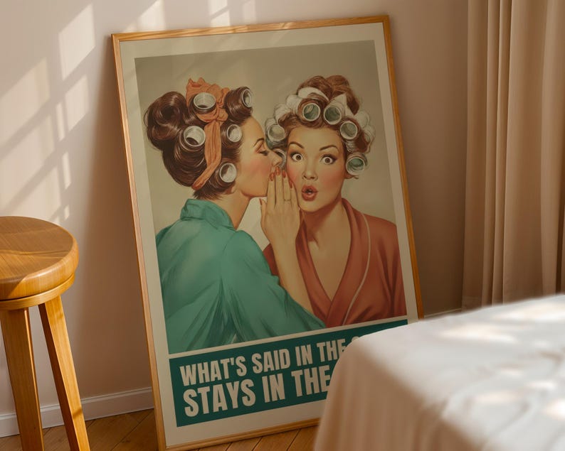 May include: A framed vintage-style poster featuring two women with curlers in their hair. One whispers to the other, who looks surprised. The poster has a teal and white banner at the bottom with the text "WHAT'S SAID IN THE STAYS IN THE".
