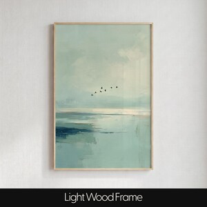 May include: A vertical wall art print in a light wood frame featuring an abstract landscape painting. The artwork displays soft shades of pale blue, teal, and white, depicting a calm body of water under a cloudy sky with a small flock of birds.